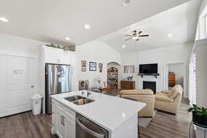 Kitchen with appliances with stainless steel finishes, a large fireplace, dark wood-style floors, light countertops, and lofted ceiling