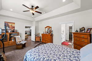 Primary bedroom with wood finished floors, a spacious walk in closet, recessed lighting, ceiling fan, and a tray ceiling