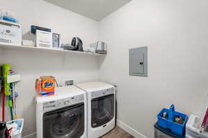 Washroom with electric panel, washer and clothes dryer, and wood finished floors