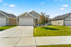 View of front of house with board and batten siding, a front lawn, a garage, stone siding, and concrete driveway