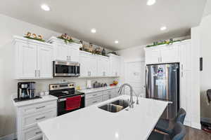Kitchen featuring appliances with stainless steel finishes, a kitchen island with sink, white cabinets, light countertops, and a kitchen breakfast bar