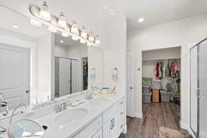 Primary full bathroom with a spacious closet, a stall shower, water closet, double vanity, and wood finished floors