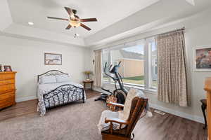 Primary bedroom featuring a tray ceiling, wood finished floors, a ceiling fan, and recessed lighting