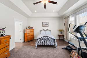 Primary bedroom featuring dark wood-style floors, a tray ceiling, recessed lighting, and a ceiling fan