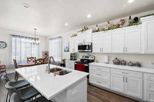 Kitchen featuring appliances with stainless steel finishes, dark wood-style flooring, a breakfast bar, a chandelier, and white cabinetry
