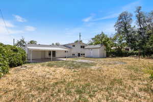 Rear view of property with a patio, a storage unit, a yard, and a carport