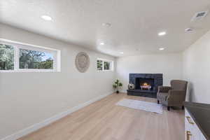 Sitting room with light wood-style floors, a fireplace, recessed lighting, and a textured ceiling