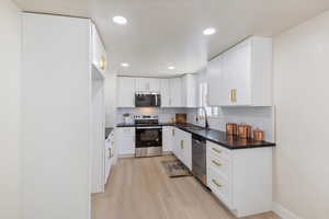 Kitchen featuring stainless steel appliances, light wood-style floors, dark countertops, white cabinets, and recessed lighting