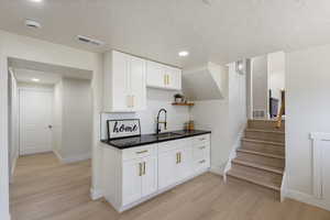 Kitchen with light wood finished floors, white cabinets, a textured ceiling, dark countertops, and open shelves