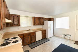 Kitchen with white appliances, under cabinet range hood, light countertops, and light floors