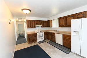 Kitchen with white appliances, under cabinet range hood, light countertops, and a textured ceiling