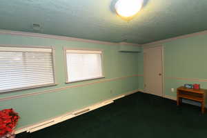 Unfurnished room with dark colored carpet, a textured ceiling, and crown molding
