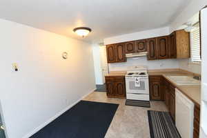 Kitchen featuring white appliances, light countertops, light flooring, under cabinet range hood, and a textured ceiling