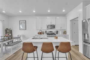 Kitchen featuring stainless steel appliances, light wood finished floors, a kitchen bar, light countertops, and a center island with sink