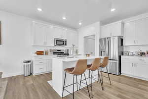 Kitchen with stainless steel appliances, a breakfast bar, light countertops, light wood-style flooring, and a kitchen island with sink