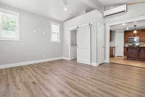 Unfurnished living room featuring a wall unit AC, a barn door, ceiling fan, light wood finished floors, and recessed lighting