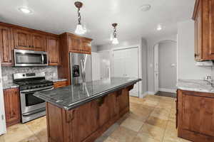 Kitchen featuring stainless steel appliances, arched walkways, decorative backsplash, stone countertops, and hanging light fixtures