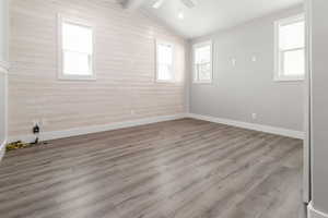 Unfurnished room with wood walls, a ceiling fan, healthy amount of natural light, and wood finished floors