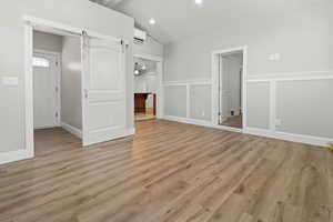 Unfurnished bedroom featuring light wood-style flooring, vaulted ceiling, a decorative wall, ensuite bathroom, and recessed lighting