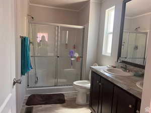 Full bath featuring a stall shower, wood finished floors, ornamental molding, and double vanity