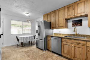 Kitchen with stainless steel appliances, brown cabinetry, dark countertops, a textured ceiling, and decorative light fixtures