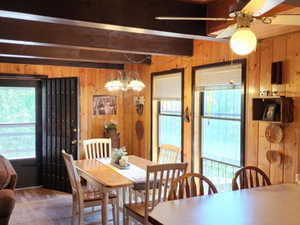 Dining space featuring wooden walls, beam ceiling, ceiling fan, a chandelier, and wood finished floors