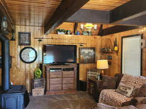 Carpeted living room featuring wood walls, a wood stove, a chandelier, and a wood ceiling with exposed beams