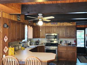 Kitchen featuring appliances with stainless steel finishes, beam ceiling, ceiling fan, light countertops, and a peninsula