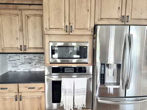 Kitchen with stainless steel appliances, light brown cabinets, tasteful backsplash, and dark countertops