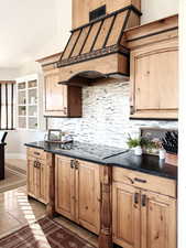 Kitchen with decorative backsplash, dark countertops, black electric cooktop, custom exhaust hood, and tile patterned floors
