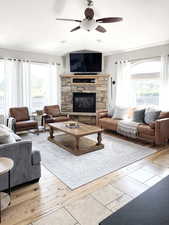 Living area with a ceiling fan, light wood-style flooring, and a stone fireplace