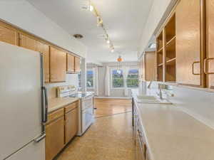 Kitchen featuring white appliances, light countertops, brown cabinetry, light wood-type flooring, and track lighting