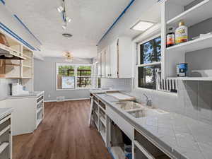 Kitchen featuring open shelves, tasteful backsplash, wood finished floors, and white cabinetry