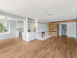 Unfurnished living room with light wood-type flooring, wooden walls, a tiled fireplace, and ceiling fan