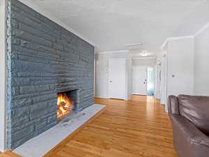 Unfurnished living room with light wood finished floors, crown molding, a stone fireplace, a textured ceiling, and attic access