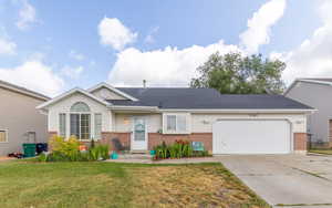 View of front facade featuring brick siding, driveway, an attached garage, and a front yard