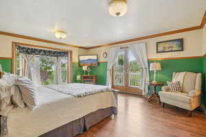 Bedroom with multiple windows, hardwood / wood-style floors, ornamental molding, and French doors to balcony