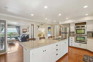 Kitchen featuring appliances with stainless steel finishes, crown molding, a kitchen island, white cabinets, and wood finished floors