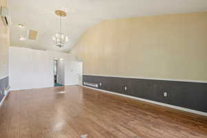 Unfurnished living room featuring a wall unit AC, a chandelier, hardwood / wood-style flooring, and vaulted ceiling