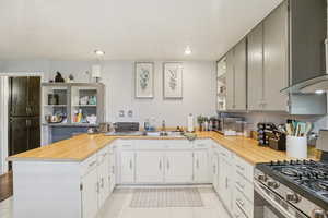 MIL - Kitchen featuring stainless steel range with gas stovetop, exhaust hood, a peninsula, open shelves, and recessed lighting