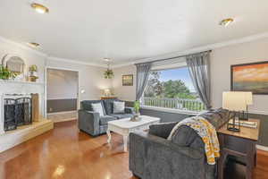 Living area with a fireplace with raised hearth, crown molding, and wood finished floors