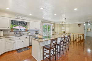 Kitchen featuring stainless steel dishwasher, crown molding, wood finished floors, a breakfast bar, and white cabinetry