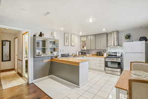 MIL - Kitchen featuring wall chimney range hood, stainless steel appliances, a peninsula, wooden counters, and recessed lighting