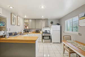 MIL - Kitchen with appliances with stainless steel finishes, wall chimney exhaust hood, wood counters, light tile patterned floors, and a peninsula