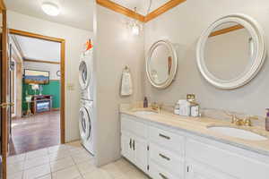 Full bathroom featuring ornamental molding, stacked washer and clothes dryer, double vanity, and tile patterned floors