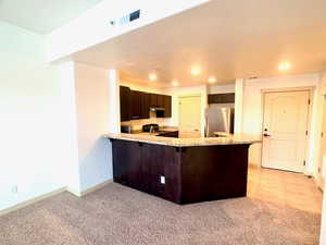 Kitchen with freestanding refrigerator, dark brown cabinets, a peninsula, recessed lighting, and light granite counter tops