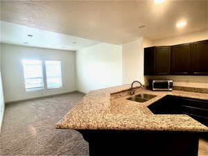 Kitchen with stainless steel microwave, light stone countertops, light colored carpet, dark brown cabinets, and recessed lighting