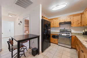 Kitchen featuring appliances with stainless steel finishes, under cabinet range hood, light tile patterned flooring, and light stone counters