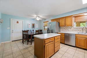 Kitchen featuring appliances with stainless steel finishes, a ceiling fan, backsplash, light countertops, and brown cabinets