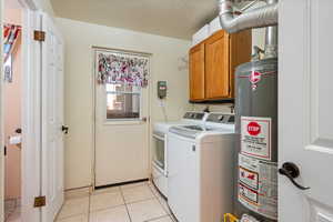 Washroom featuring cabinet space, gas water heater, washing machine and clothes dryer, and light tile patterned floors